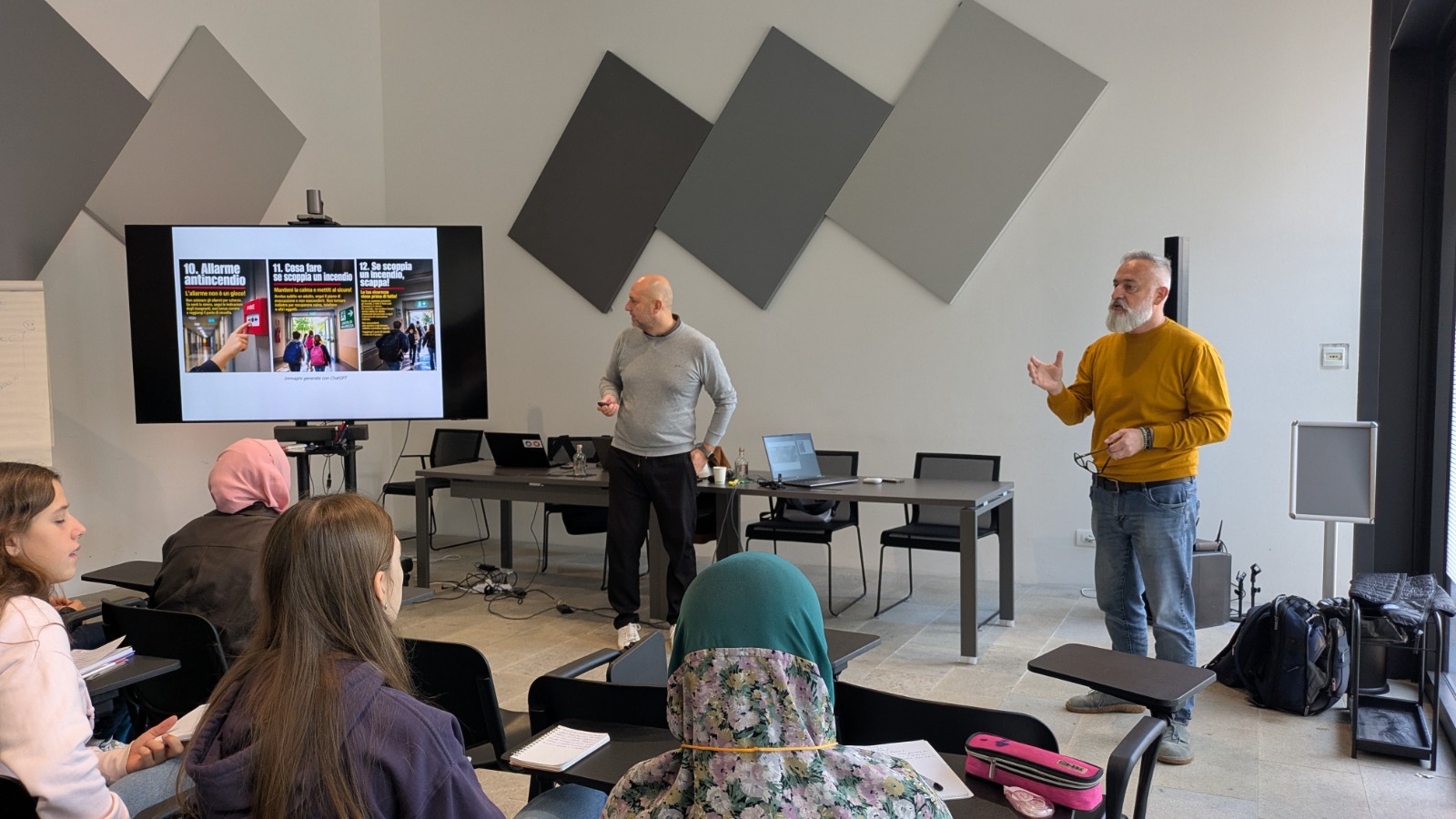 Un incontro di formazione con un relatore che spiega procedure di sicurezza antincendio, mentre gli studenti ascoltano. Un proiettore mostra informazioni visive sulle procedure.